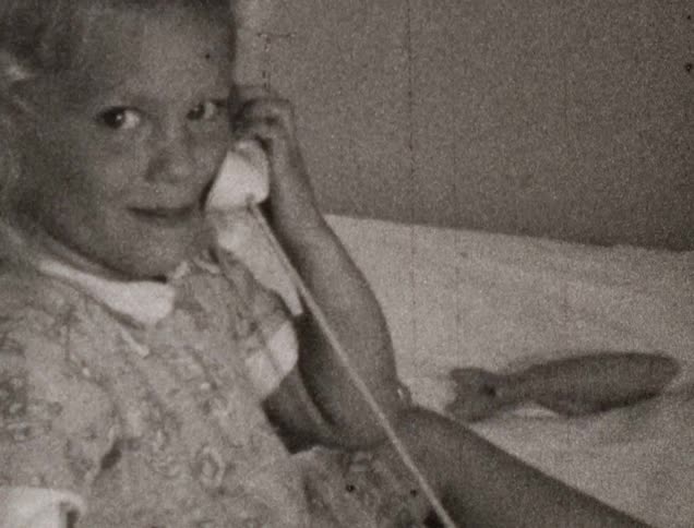 A young blonde toddler sits in a bed and plays with a toy phone