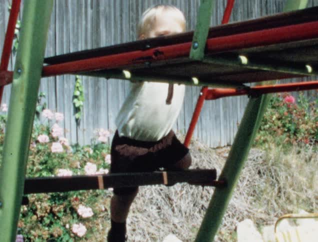 A little white boy clutches a camera as he climbs a ladder on a slide