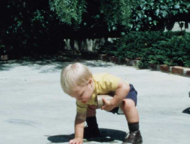 A young boy picks up rocks that keep falling from his cup