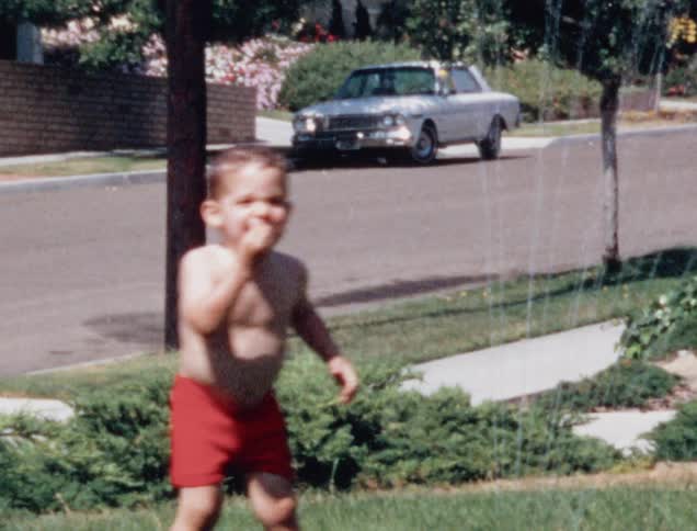 A boy soaks his face in the sprinkler