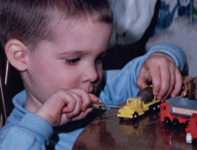 Kid plays with toy cars and tries to turn screws with a screwdriver
