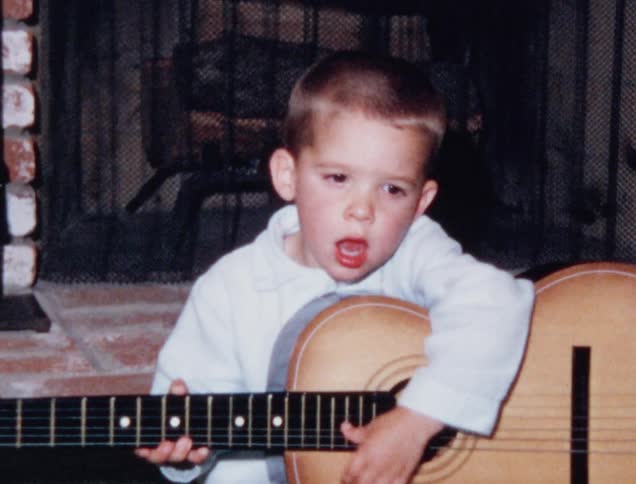 Little child plays a guitar in front of the fireplace at home