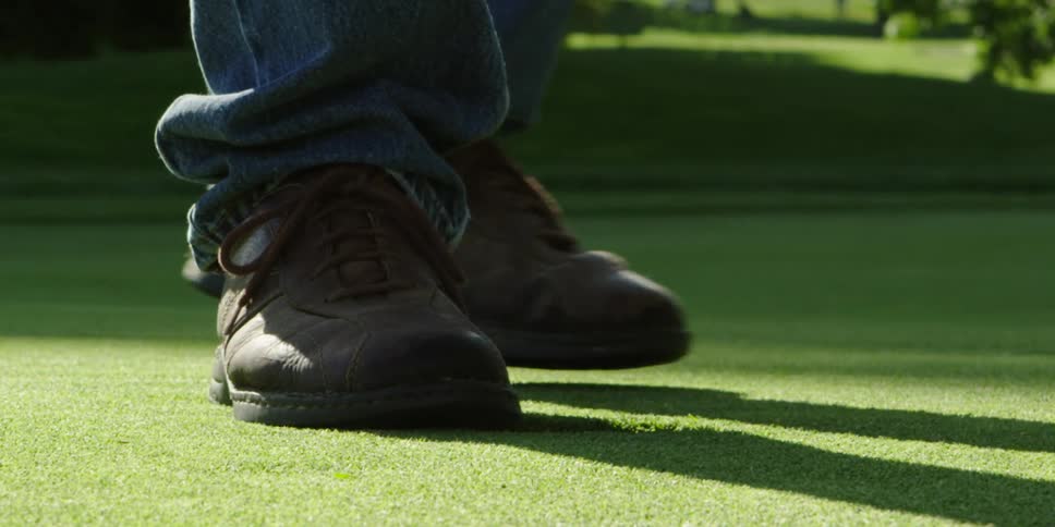 A man stands on a freshly manicured lawn in denim with brown shoes