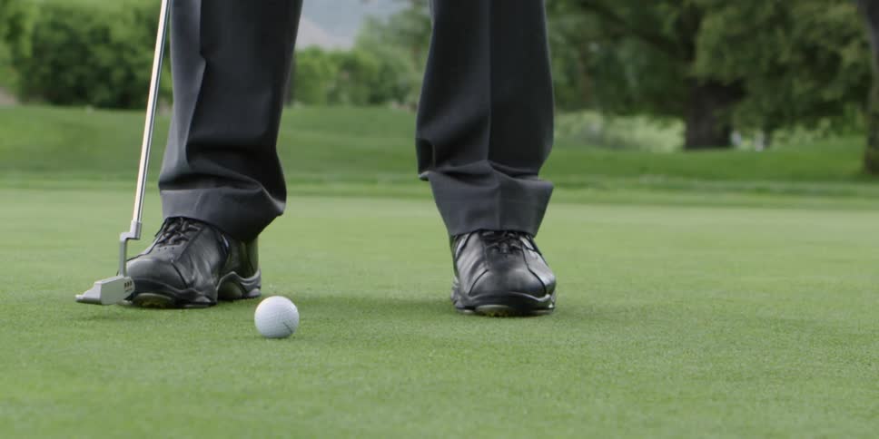 Man standing on golf court drops a golf ball in front of a golf club