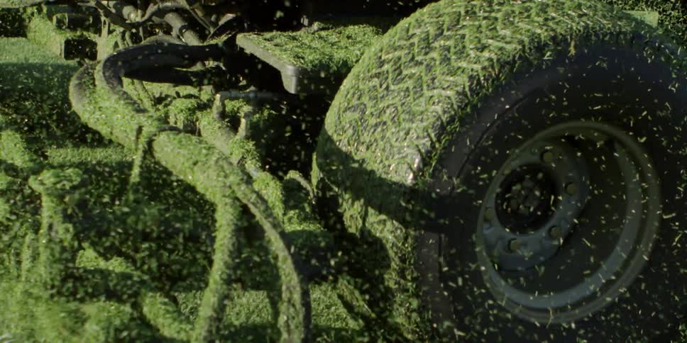 A large lawn mower is covered in grass as particles fly everywhere