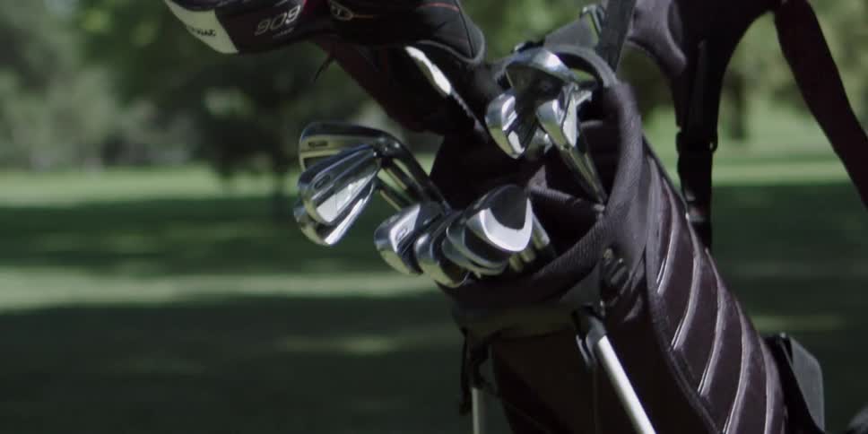 Male grabs the strap of a golf club bag that is on the fairway of the golf course and pick it up and carries it away