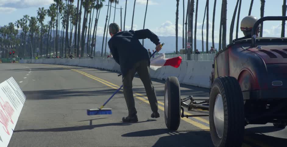 Man uses a broom to sweep the racetrack in front of a vintage race car