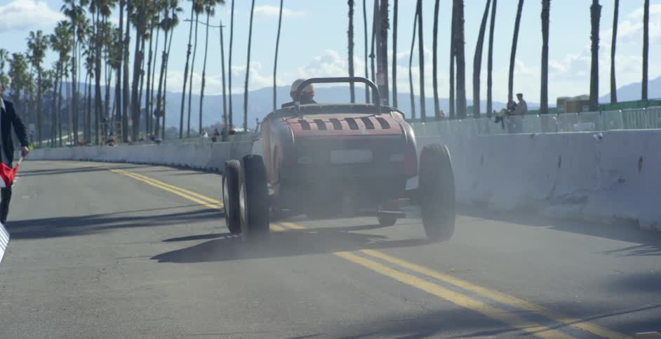 Two men in race cars tear down a city street as a crowd watches