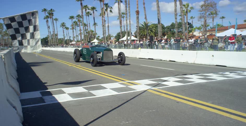 A checkered flag hangs over a concrete barrier as a racing car drives down a city street