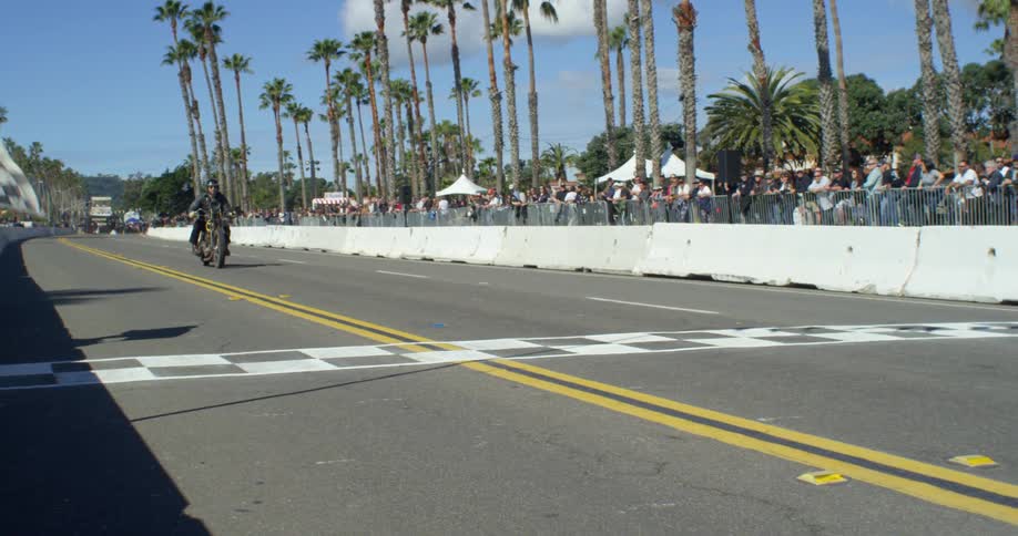 Men ride motorcycles on a raceway as a crowd watches