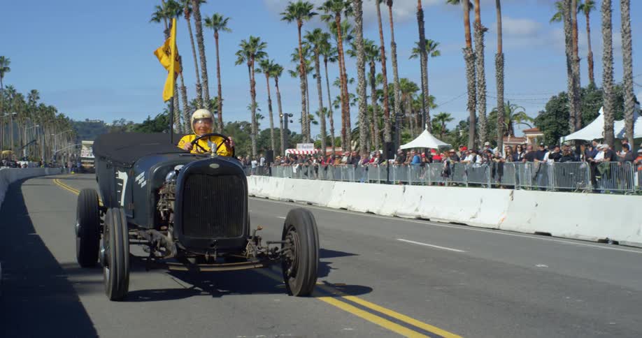 A man drives a vintage car as spectators watch
