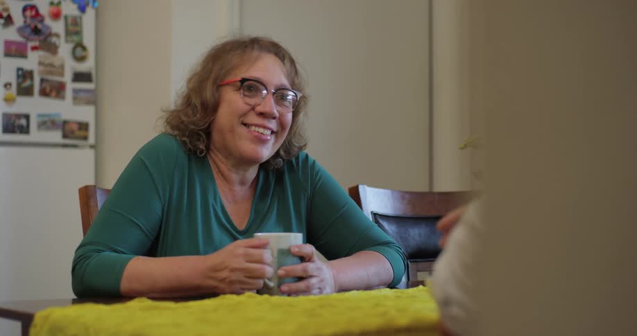 A woman has a conversation with someone across the kitchen table from her