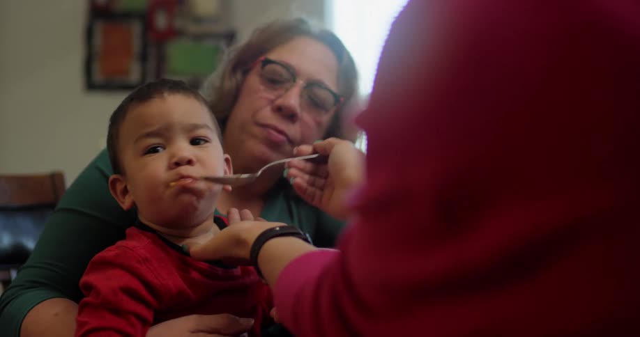 A baby tries to refuse to eat as hes held by his grandmother