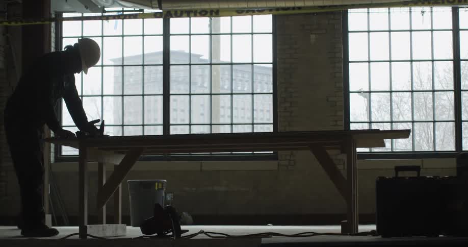 A construction worker moves around a tool sitting on a wooden table at a job site