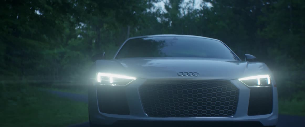 A silver car drives down the road with its headlights on
