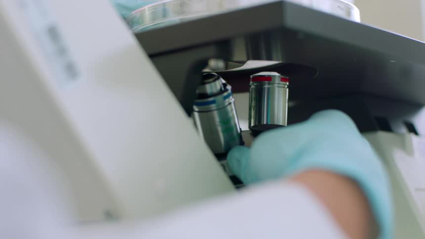 A person in a lab coat and gloves twisting a component on a large scientific device