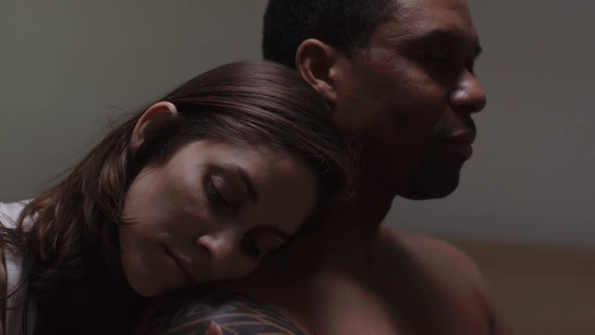 A woman walking up behind a man and resting her head on his shoulder