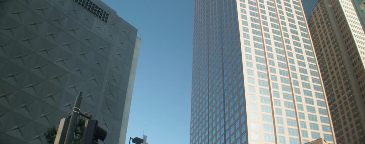 Skyscraper windows reflect neighboring skyscraper above traffic lights under clear blue sky
