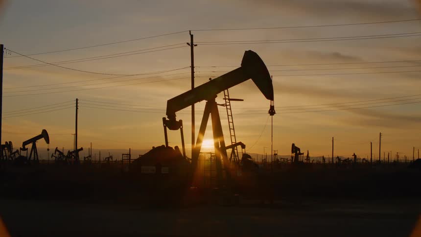 An oil drilling machine is silhouetted against the sunlight and digs for oil in the oilfield