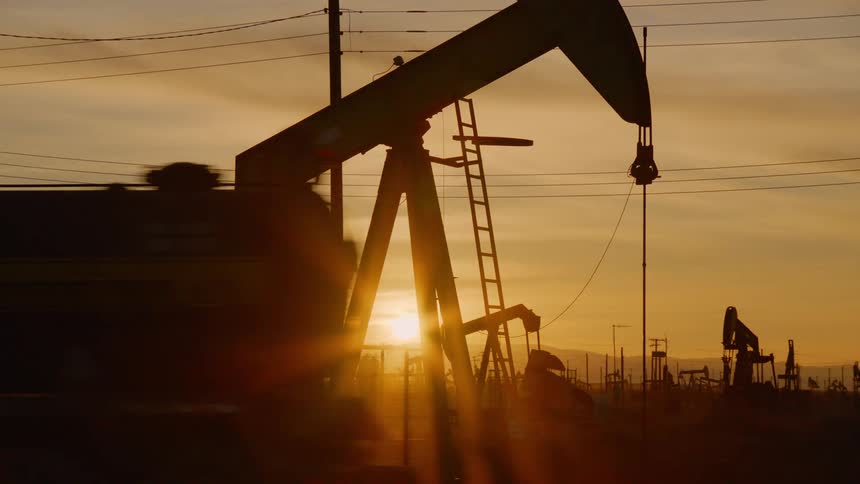 Silhouette of a pumpjack on an oil drilling site at sunset as a truck drives by