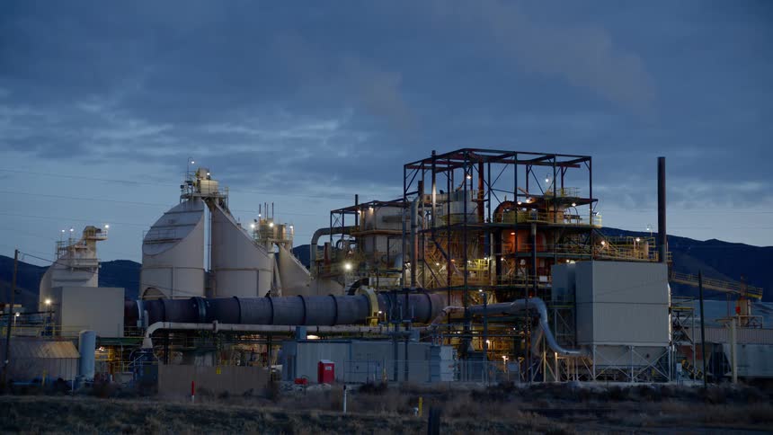 A refinery with chimneys and smoke with the sky in the background