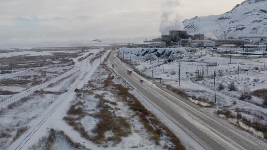 Traffic moves down a highway in a rural area near a small town and a large refinery