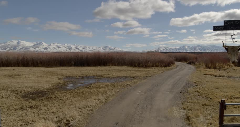 An open gate gives access to a dirt road that leads to a snow covered mountain range