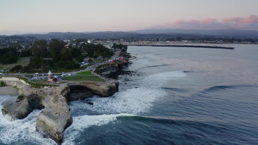 Traffic from sprawling city flows along highway bordering ocean as waves crash on shore