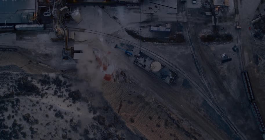 Smoke billowing from a factory next to a train track in the evening
