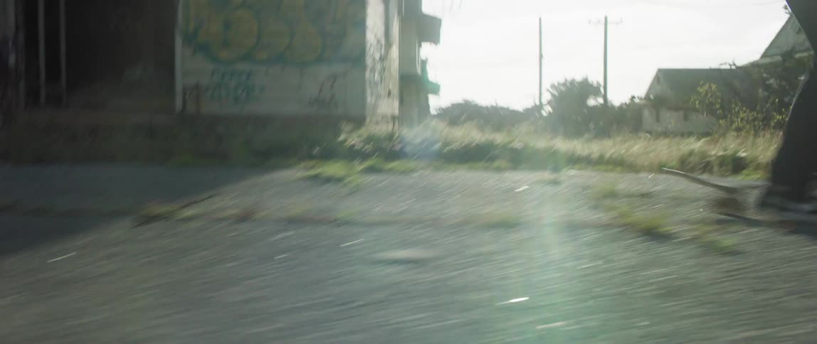 Two men run fast and start skateboarding in the street passing the houses with graffiti