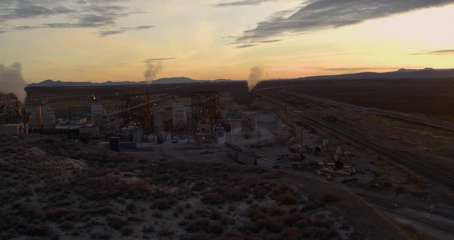 Smoke billows out of several smokestacks at a refinery in a rural area