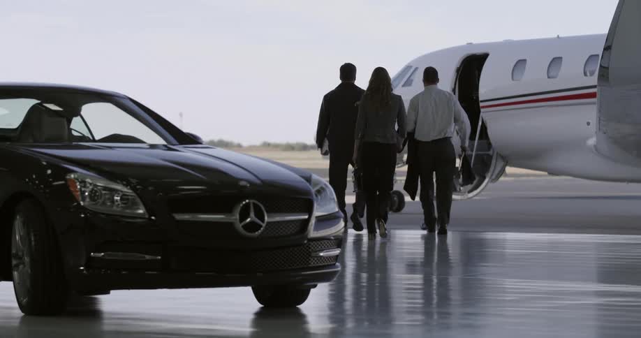 Three people walk from a car to the door of a private jet