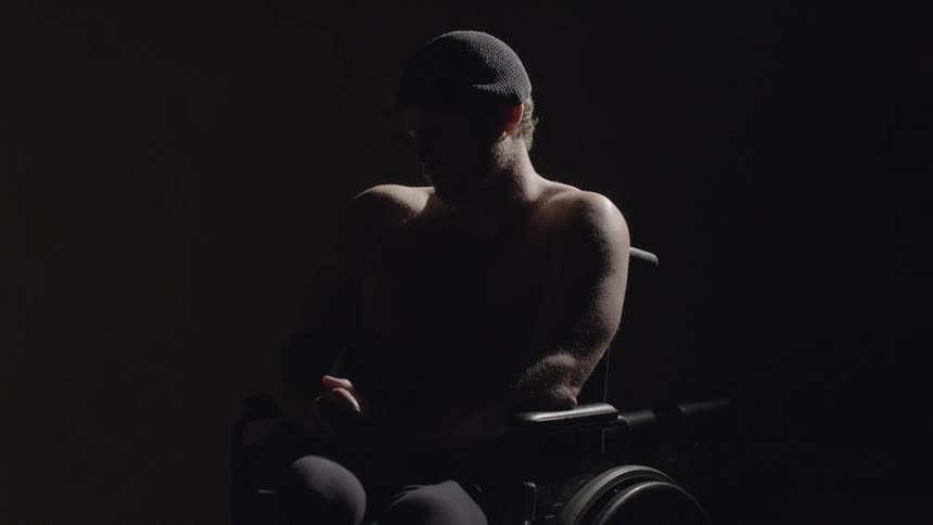 A man sits in a wheelchair in a dark room