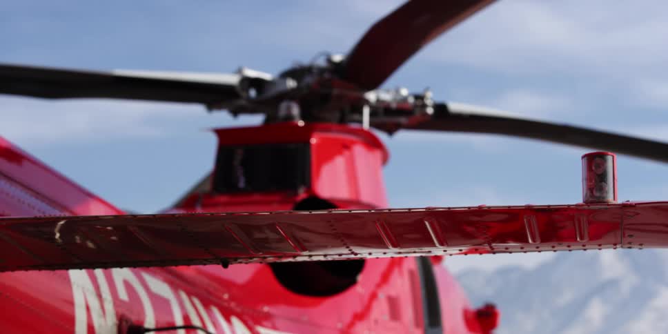 Red helicopter sits with snowy mountains in the distance