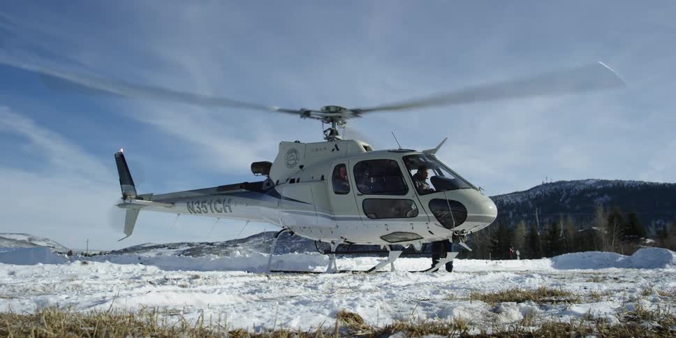Helicopter with spinning rotor grounded on the snow near a mountain