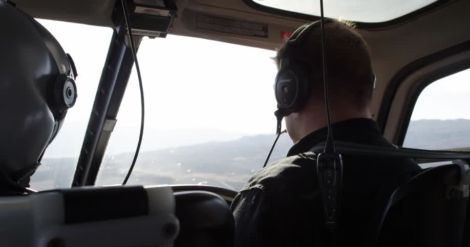 A helicopter with two people flies over a rural area