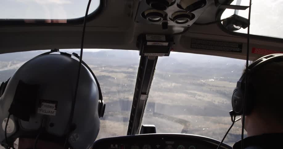 Two white males pilot a helicopter over a rural area
