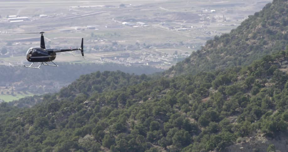 A helicopter flying in the sky over trees with towns in the background