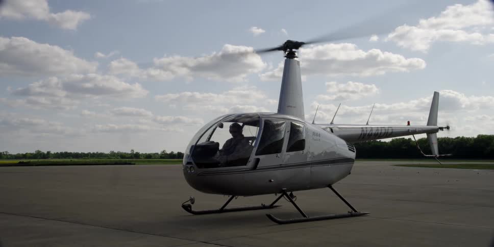 Helicopter sits on flat lot lined by trees under cloudy sky
