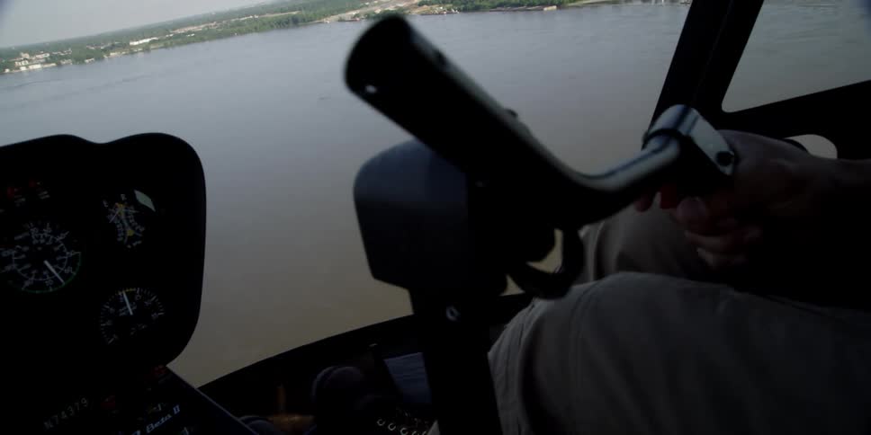 A man operating a helicopter flying over a river