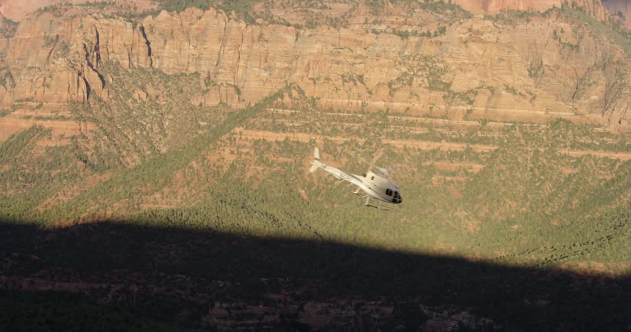 A helicopter flies downward and past a neighborhood at the base of a canyon