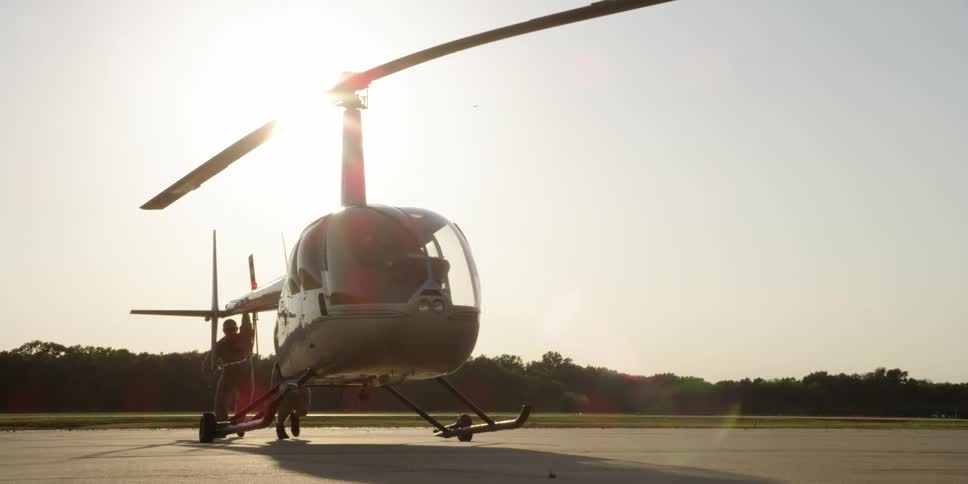 Two men lift a small helicopter off the ground