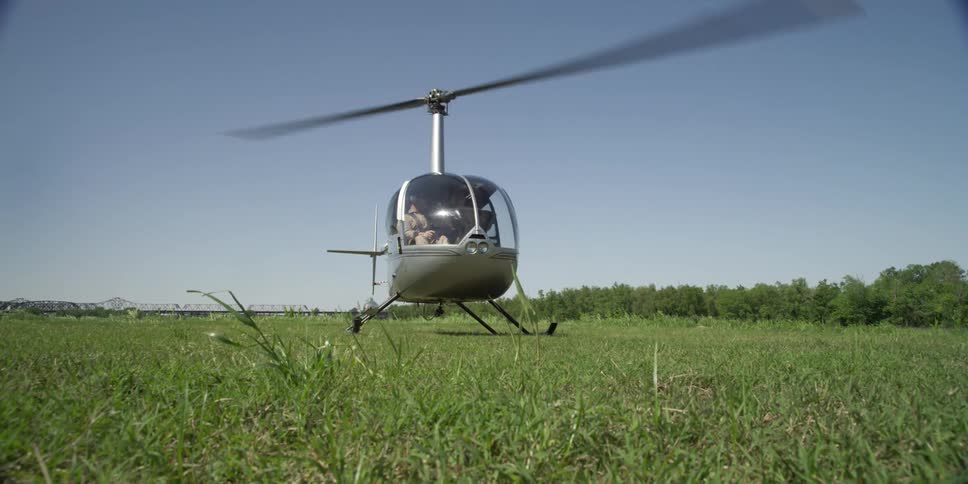 A helicopter with blades spinning sits in a grassy field