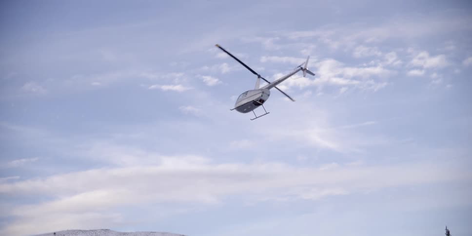 Helicopter flies over the trees near the snowy mountains