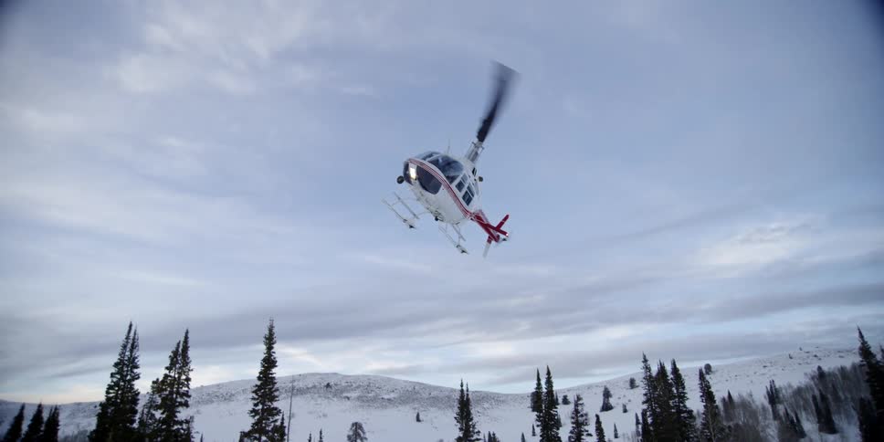 A helicopter flies over a snow covered forest and plain