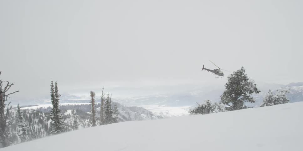 Helicopter flies over snow covered mountains
