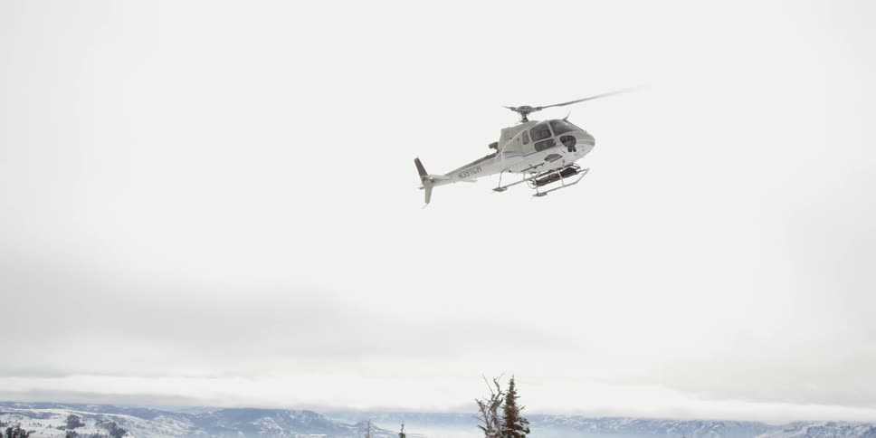 A helicopter flies over mountains during the winter