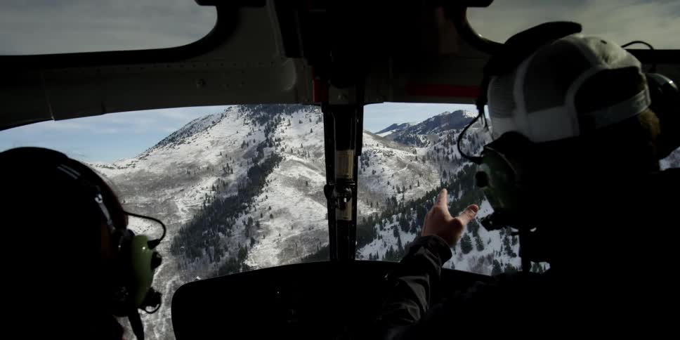 Two men are flying a helicopter over the mountains