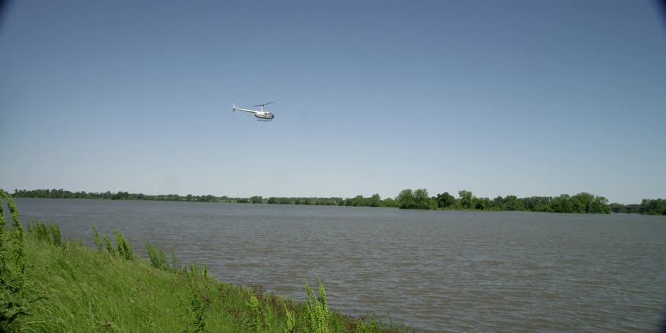 A helicopter flying over a river with trees and the sky in the background