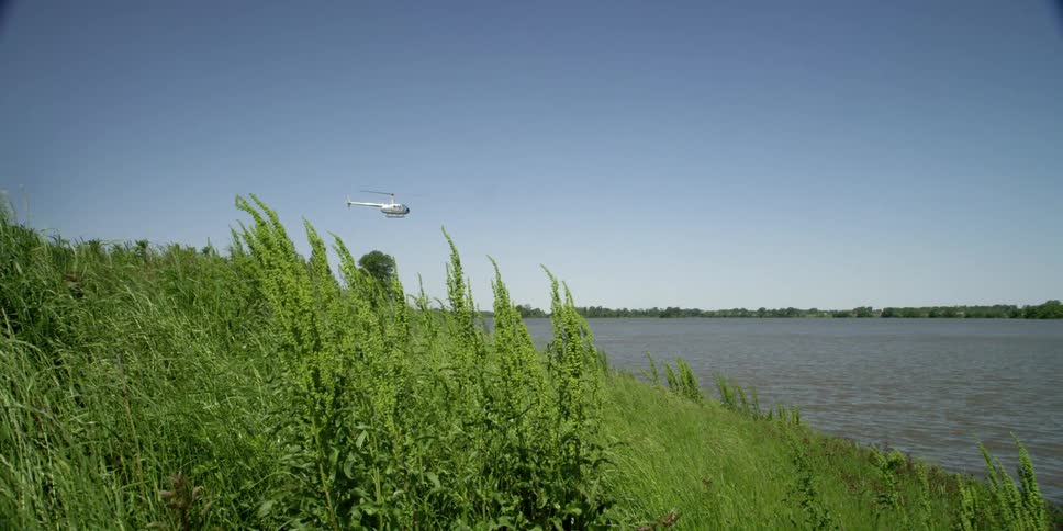 A helicopter flying over a river with trees and the sky in the background